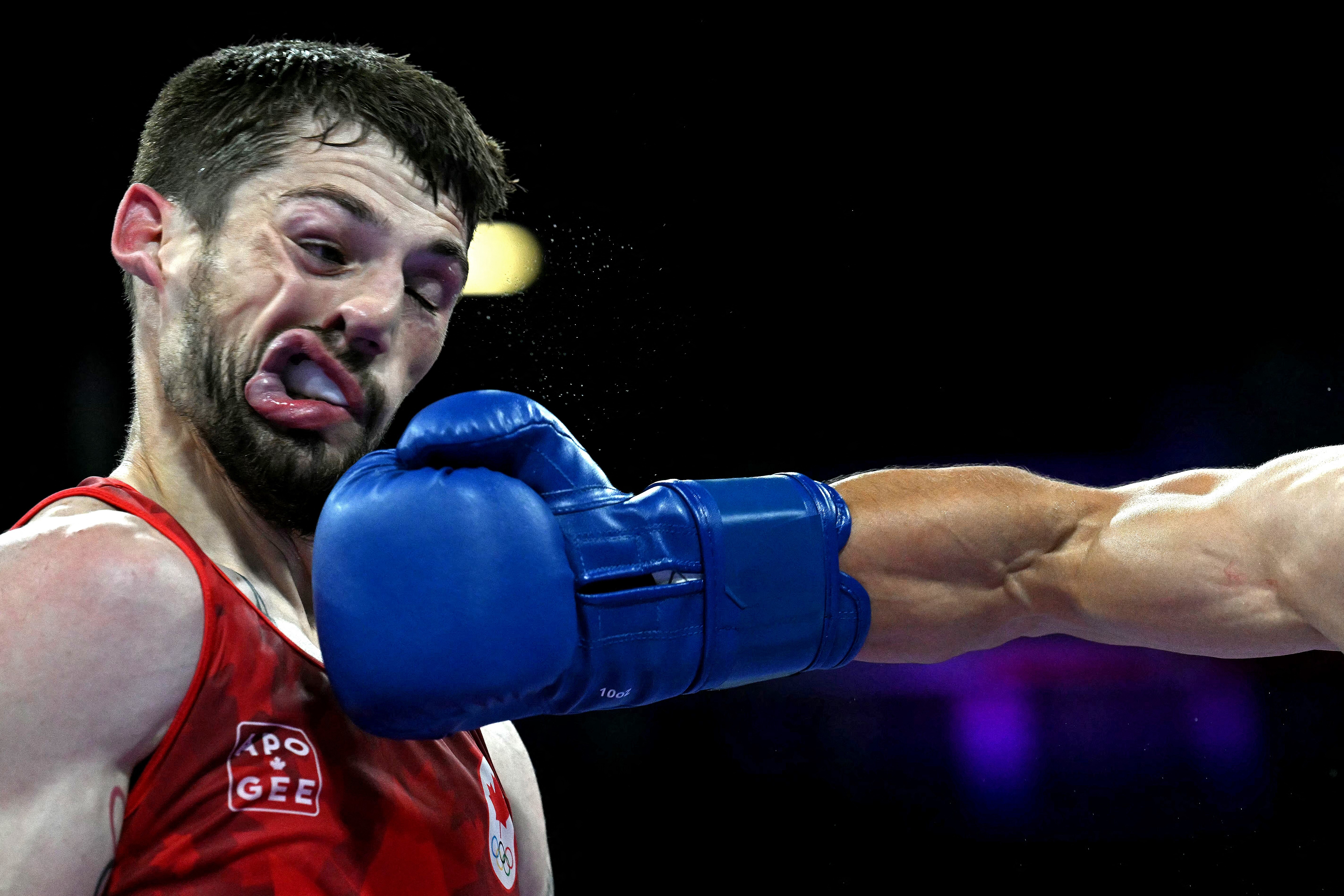 A boxer's contorted face, seen just after being punched hard, with his opponent's arm and glove below