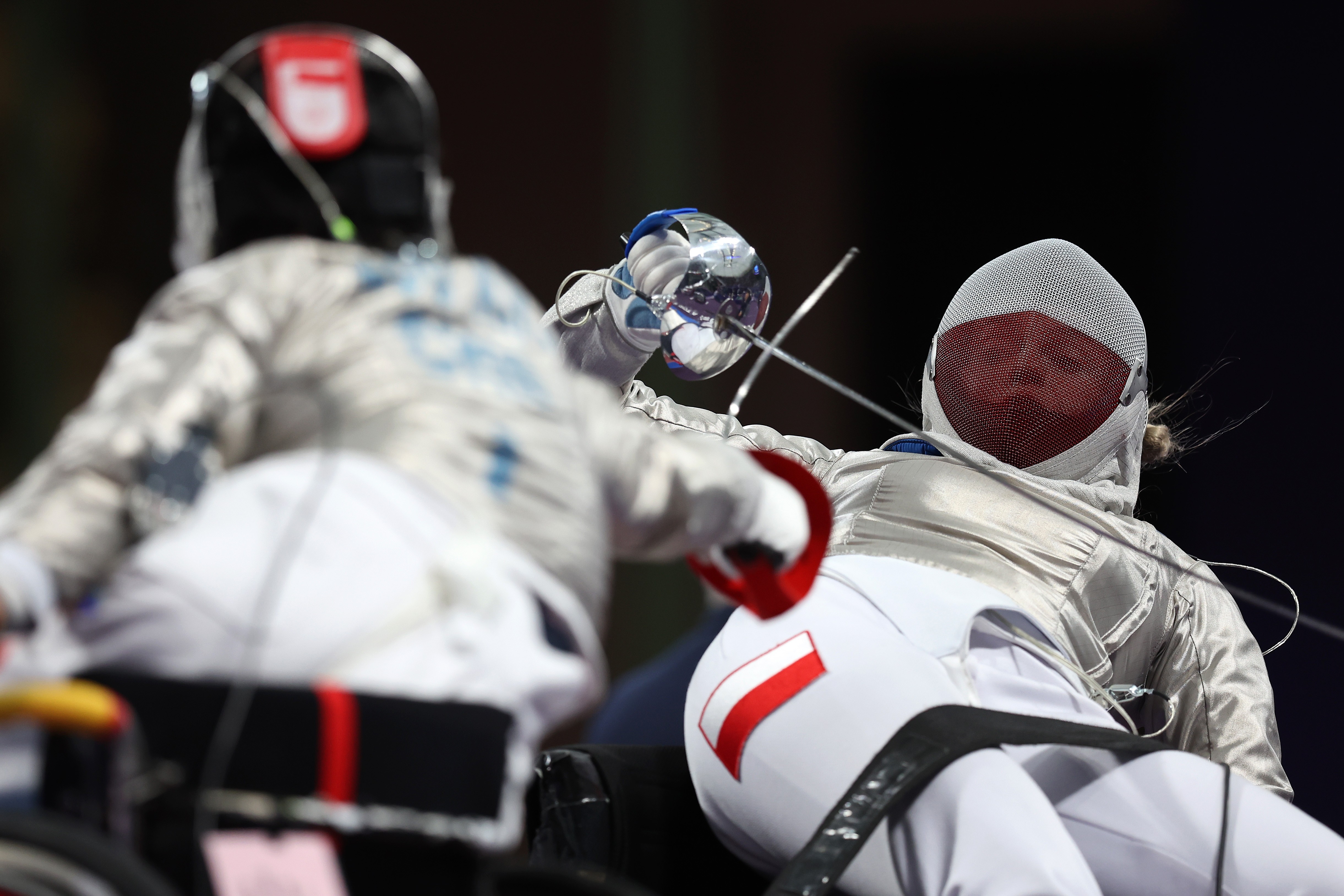 A wheelchair fencer leans far back while deflecting an attack from another fencer.