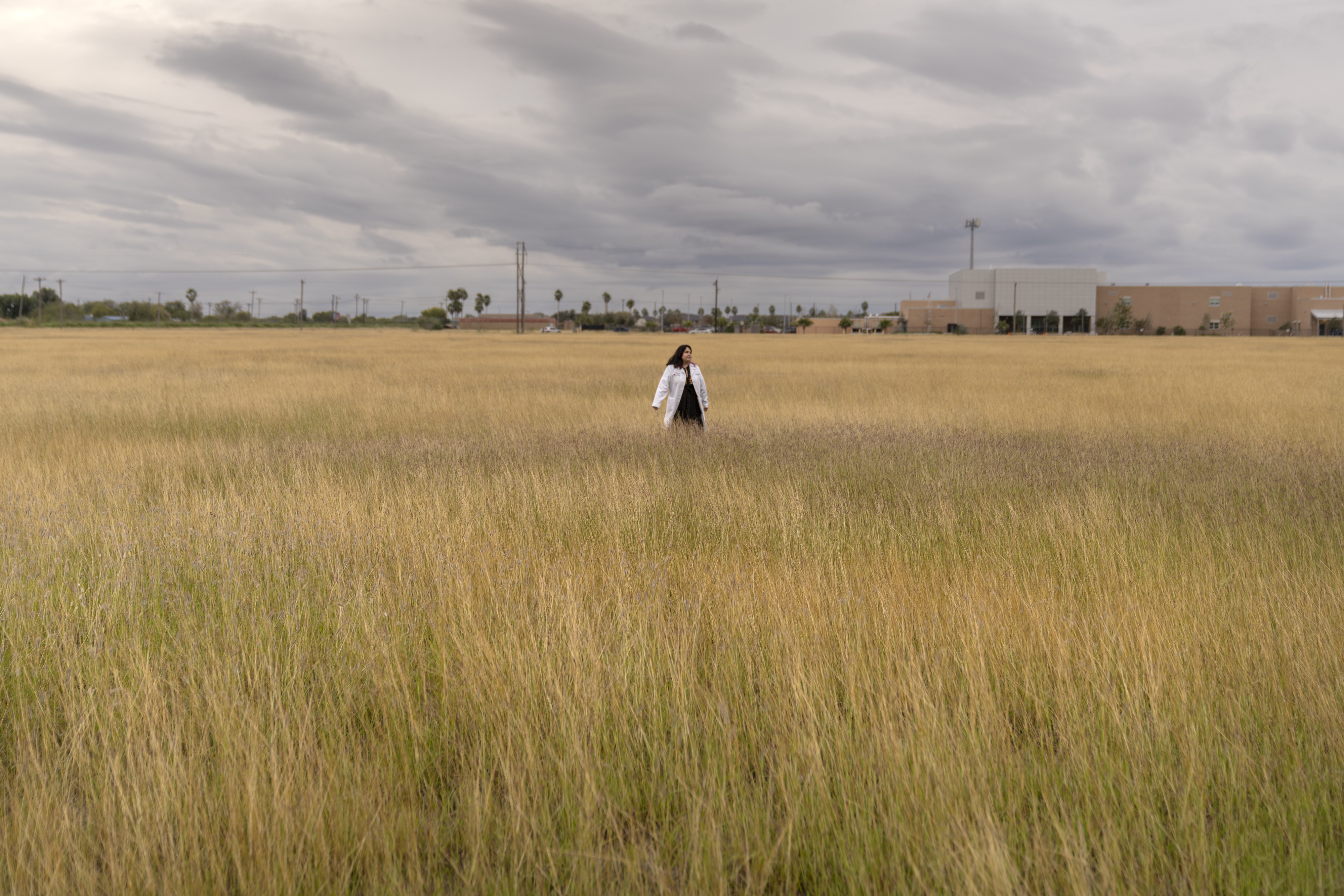 A photograph of Gladys Maestre walking through a grassy field outside the neuroscience institute at the University of Texas at Rio Grande Valley in Harlingen, Texas