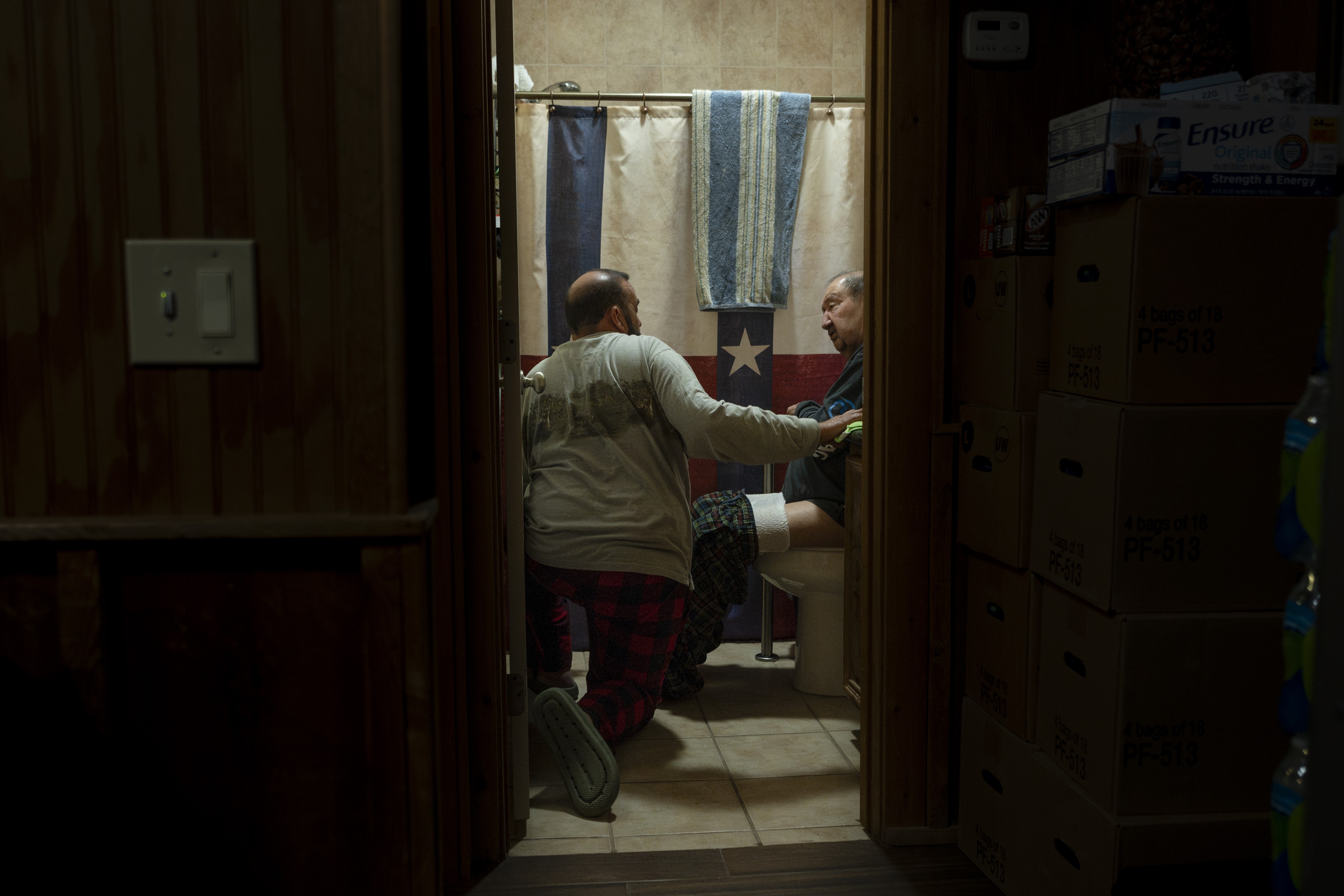 A photograph of Juan 'Manny' Saenz helping his father, Francisco 'Pancho' Saenz, use the bathroom in Manny’s home in Rio Grande City in December 2023