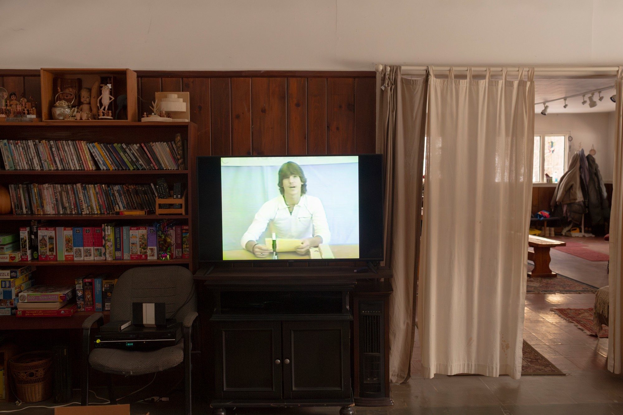 photo of living room with shelves and a TV displaying video of young man at desk giving presentation